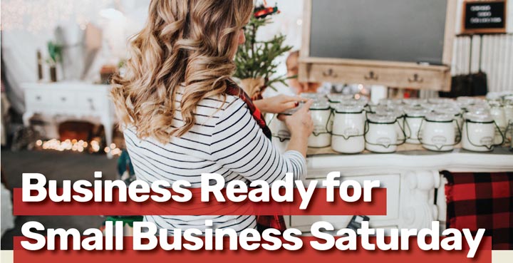 Woman tending to candle products in a shop decorated for the holidays with text Business Ready for Small Business Saturday